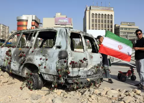 Un hombre sostiene la bandera de Ir�n cerca de un carro destruido tras el bombardeo de Israel, Teher�n, 23 de junio de 2025.
