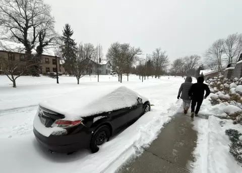 Dos personas caminan al lado de una calle afectada por la nieve este domingo en la ciudad de Hudson, Ohio (EE.UU.)